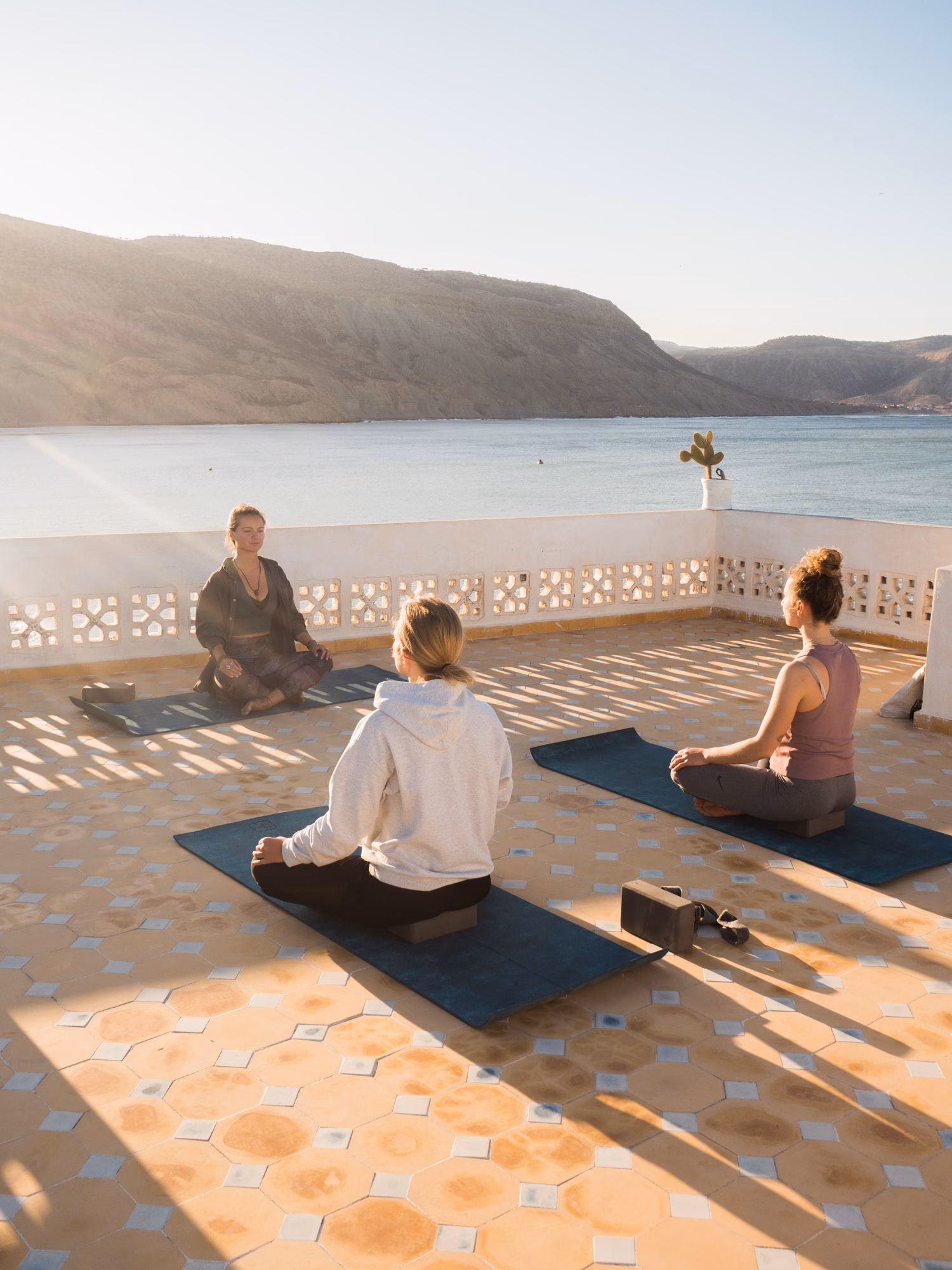 Izabella leading a seated meditation on a sunlit terrace above the ocean