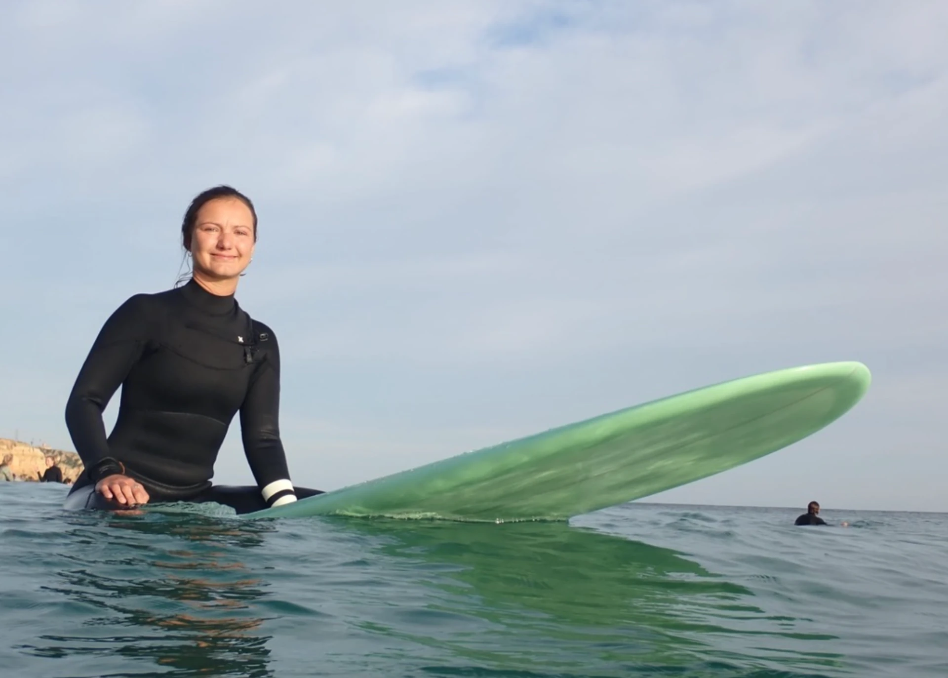 Izabella in a wetsuit, smiling on her surfboard in open water